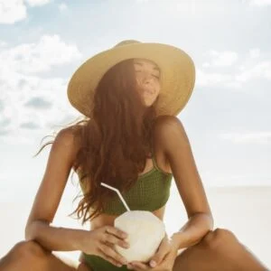 Smiling woman holding coconut on sunny tropical beach