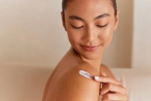 Close-up of a woman looking over her shoulder and applying lotion to tanned skin.