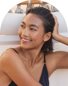 Smiling woman relaxing outdoors on a beach chair showcasing a natural-looking spray tan.