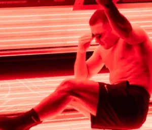 Man settling into a red light therapy bed wearing swim shorts and protective eye wear.