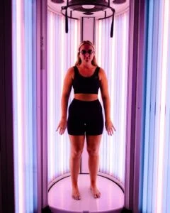 Customer using an advanced stand-up UV tanning booth after a WellFit skincare treatment at The Tanning Shop.