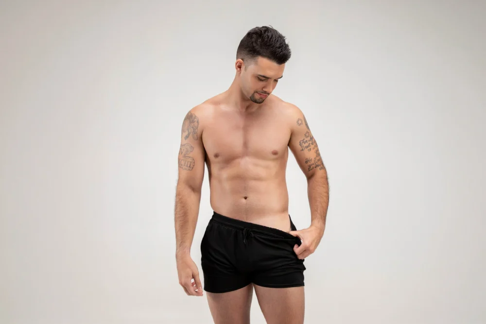 A man in black swimming trunks showing a tan line created by the Norvell clear spray tan.