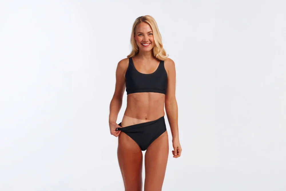 Smiling woman in black swimwear showing a noticeable tan line after getting a Norvell dark spray tan at The Tanning Shop Ireland.